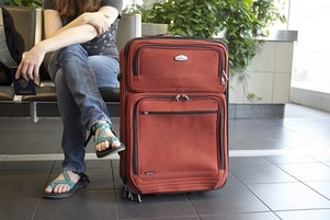 An airport traveler in sandals in sitting next to their travel luggage.